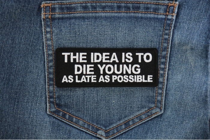 The Idea is to Die Young as Late as Possible Patch shown on jeans