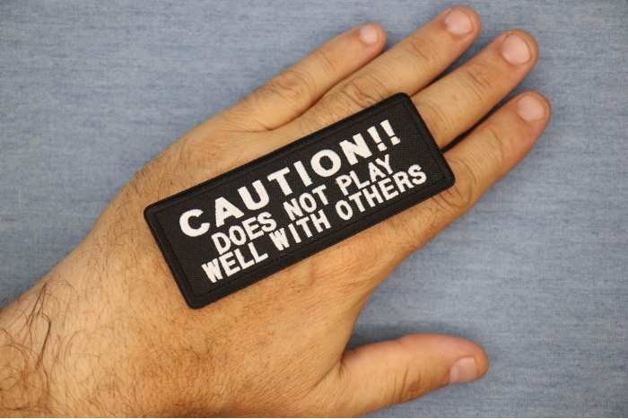 Caution Does Not Play Well With Others Funny Iron on Patch shown on hand for size comparison