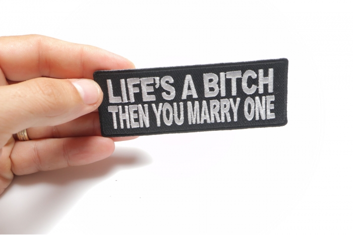 Life's A Bitch Then You Marry One Funny Iron on Patch shown on hand for size comparison