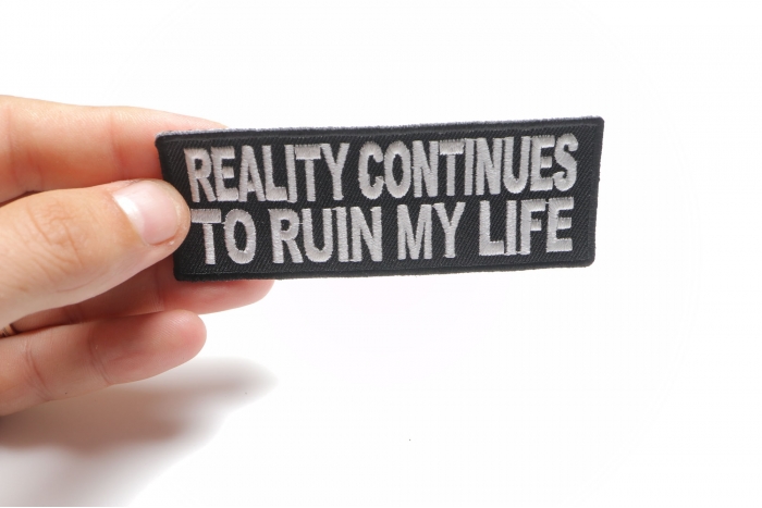 Reality Continues To Ruin My Life Funny Iron on Patch shown on hand for size comparison