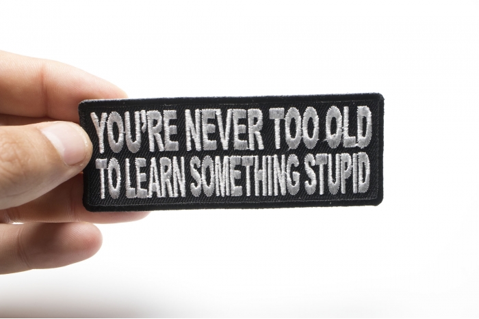 You're Never Too Old To Learn Something Stupid Funny Iron on Patch shown on hand for size comparison