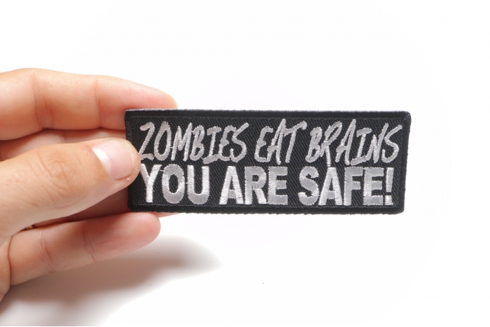 Zombies Eat Brains You Are Safe Funny Iron on Patch shown on hand for size comparison