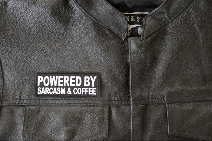 Powered By Sarcasm and Coffee Patch - 4x1.5 inch - Embroidered Iron on Patch shown on leather vest