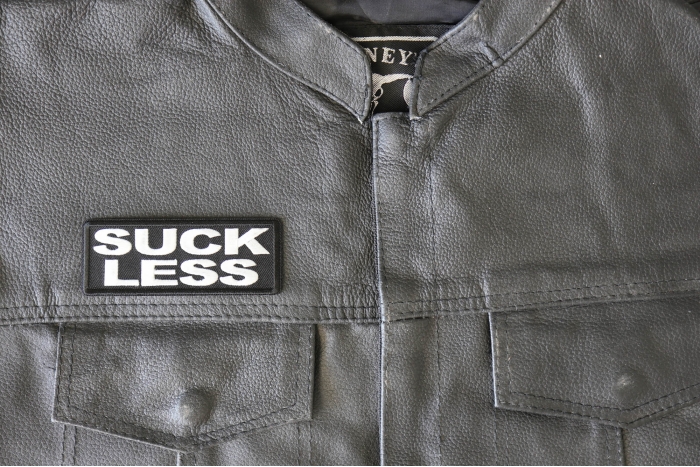 Suck Less Patch - 4x1.5 inch - Embroidered Iron on Patch shown on leather vest