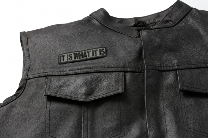 It Is What It Is Patch In Gray - 3.5x1 inch. Embroidered Iron on Patch shown on leather vest