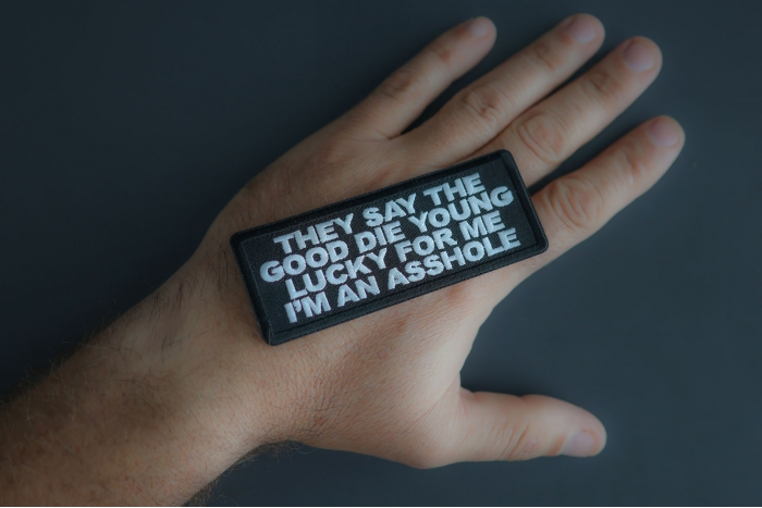 They Say The Good Die Young Lucky For Me I'm An Asshole Patch shown on hand for size comparison
