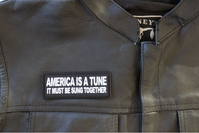 America is a Tun it must be Sung Together Patch - 4x1.5 inch - Embroidered Iron on Patch shown on leather vest