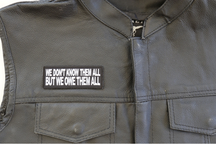 We Don't Know Them All But We Owe Them All Patch - 4x1.5 inch. Embroidered Iron on Patch shown on leather vest